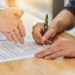 close-up-hand-holding-pen-sign-contract-document - Pratama Institute