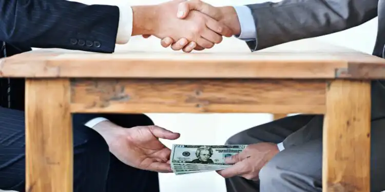 underthetable-transactions-cropped-shot-two-businessmen-shaking-hands-while-money-passes-hands-table - Pratama Institute