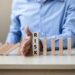 businessman-hand-stopping-falling-wooden-blocks-dominoes - Pratama Institute Era Baru Manajemen Risiko di BUMN