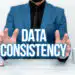 Sign displaying Data Consistency Concept meaning data values are the same for all instances of application Discussing Important Idea Presenting And Explaining Business Plan Designs - Pratama Institute Business professional in a blue suit framing glowing 'DATA CONSISTENCY' text to emphasize the concept of data integrity/consistency.
