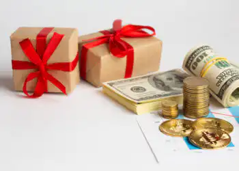 Two gift boxes with red ribbons beside rolled cash, coins, and a financial chart.