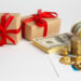 Two gift boxes with red ribbons beside rolled cash, coins, and a financial chart.