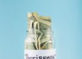 Jar filled with folded dollar bills labeled 'RETIREMENT' against a blue background, symbolizing retirement savings.
