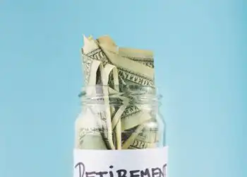 Jar filled with folded dollar bills labeled 'RETIREMENT' against a blue background, symbolizing retirement savings.