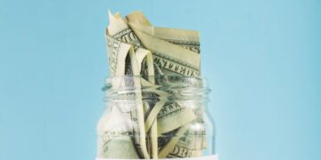 - Pratama Institute Jar filled with folded dollar bills labeled 'RETIREMENT' against a blue background, symbolizing retirement savings.