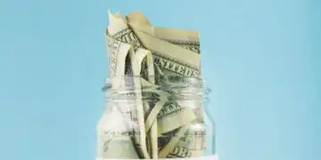 Jar filled with folded dollar bills labeled 'RETIREMENT' against a blue background, symbolizing retirement savings.