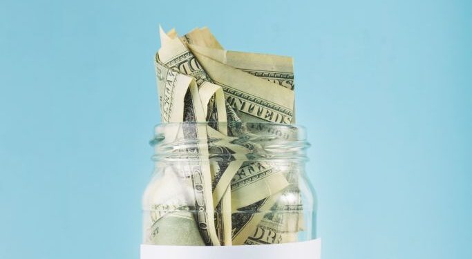 Jar filled with folded dollar bills labeled 'RETIREMENT' against a blue background, symbolizing retirement savings.