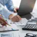 Accounting company provide finance and taxation for profit income Insight - Pratama Institute Team of professionals reviewing charts and documents around a desk with a calculator and laptop nearby, in a meeting room.